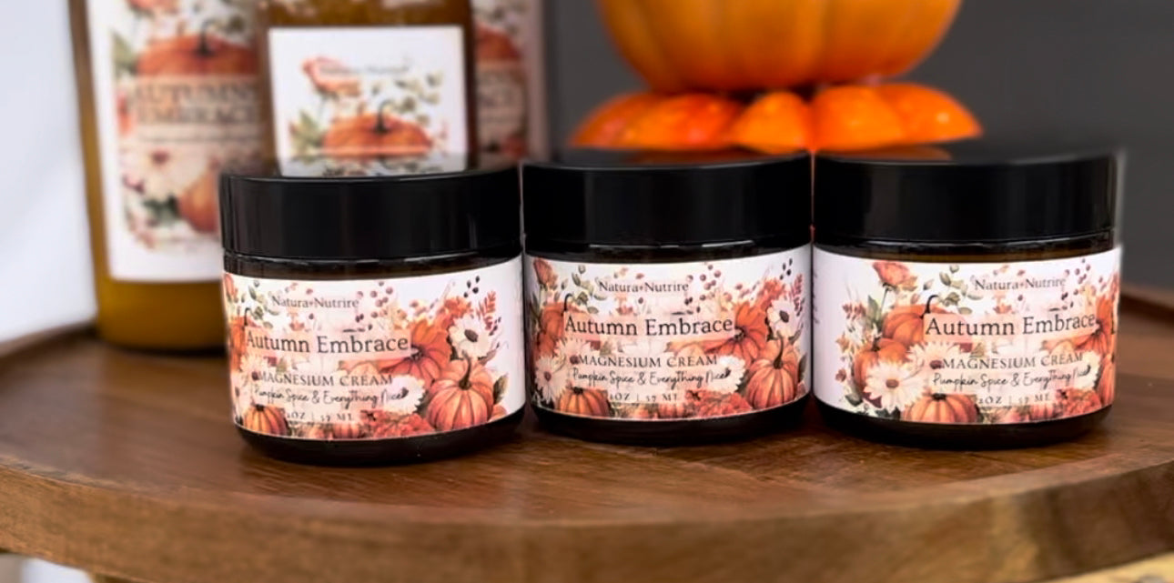 Jars of Natura+Nutrire magnesium cream with autumn-themed labels, displayed on a wooden shelf with decorative items in the background.