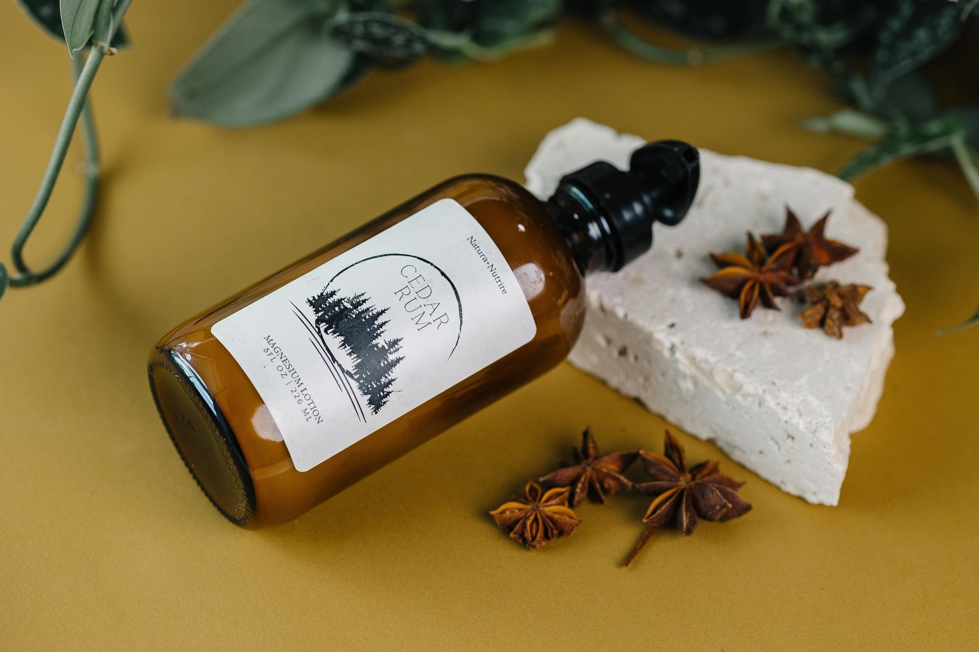 Brown bottle with a label next to a white bar of soap and star anise on a yellow background