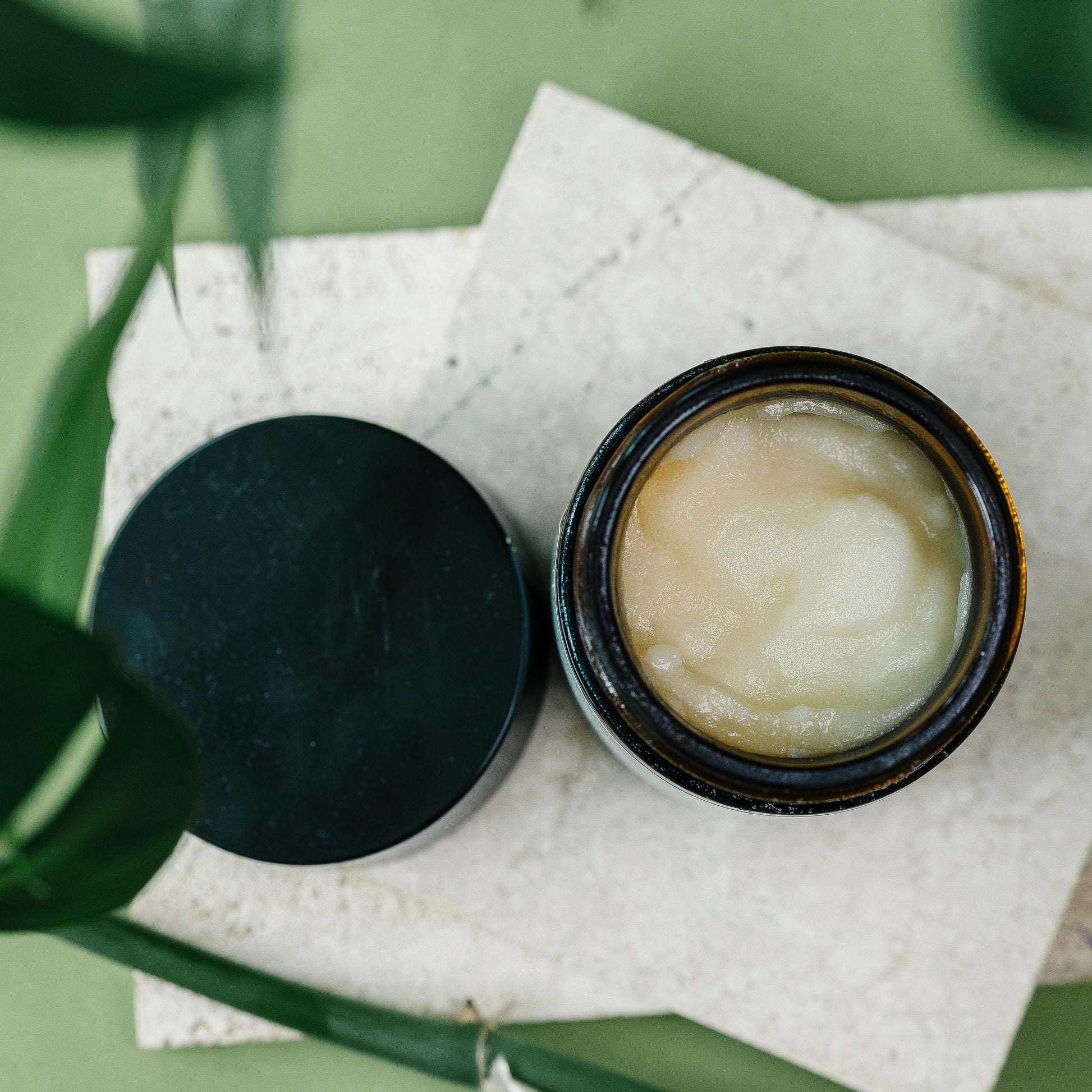 Small jar of cream on a white napkin with green leaves in the background