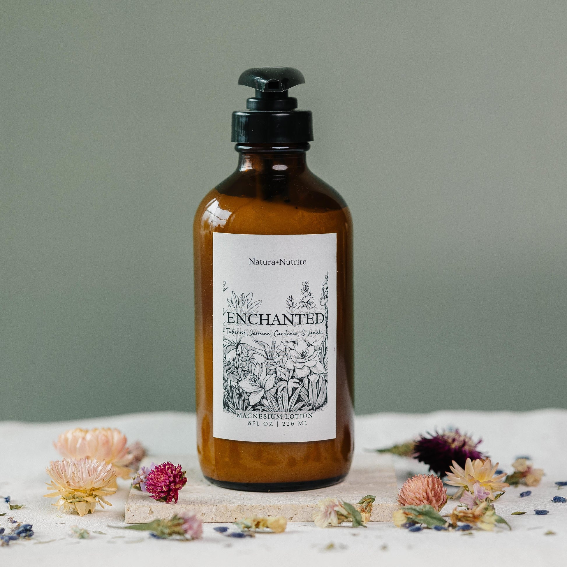 Brown bottle labeled 'Enchanted' with flowers on a light surface and gray background