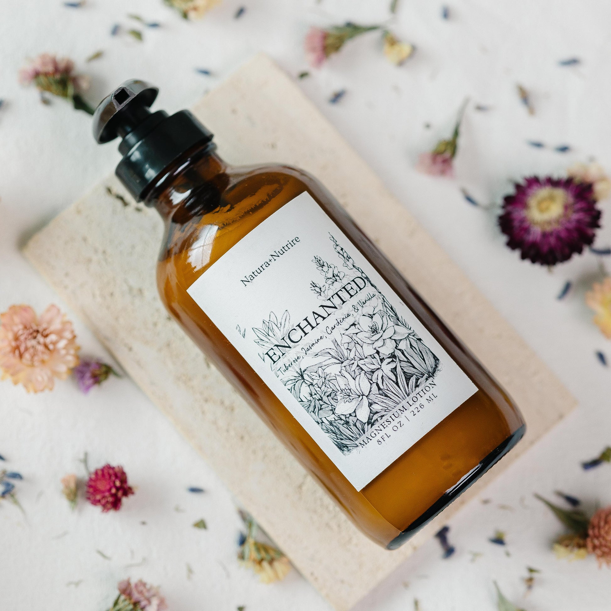 Bottle of 'Enchanted' product on a textured surface with flowers