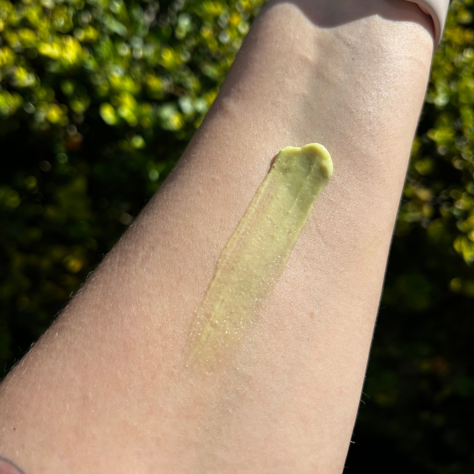 Green cream applied to a person's arm with a blurred green outdoor background
