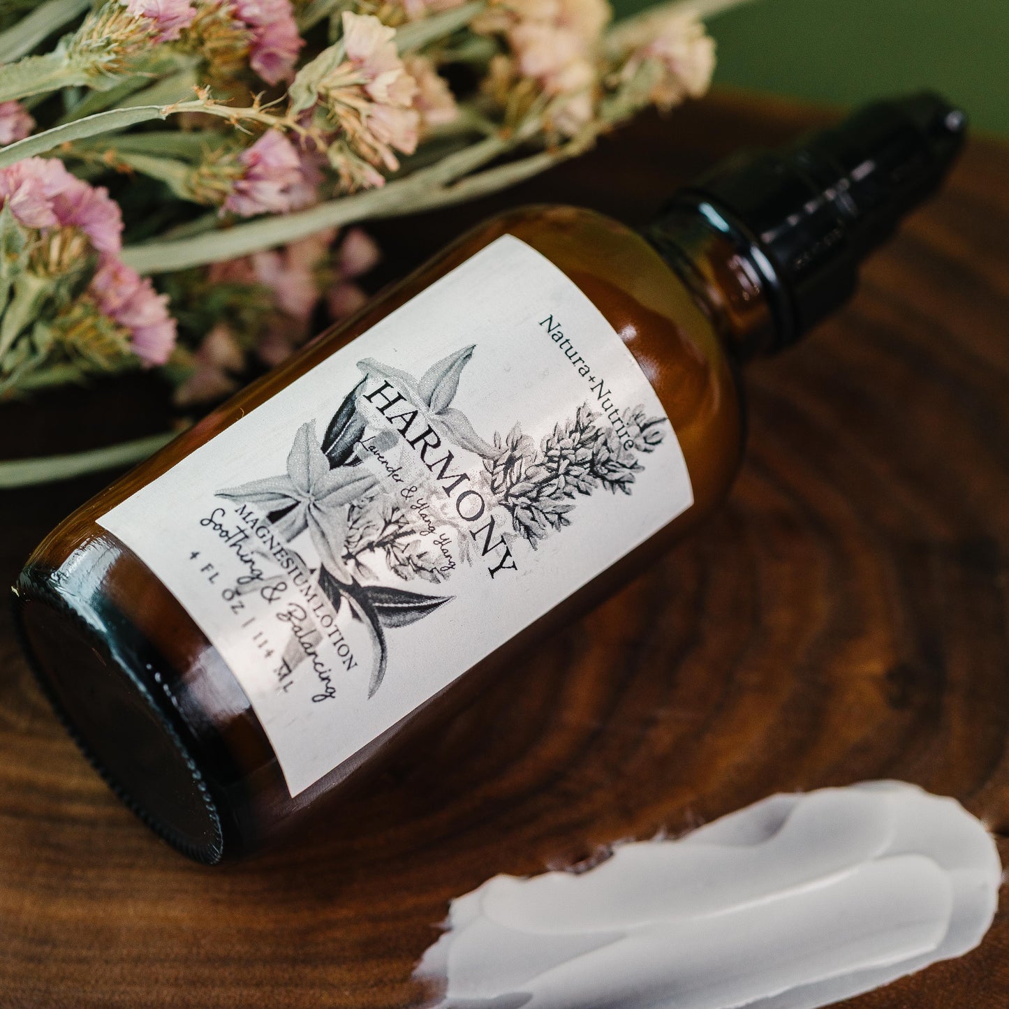 Brown bottle with a label on a wooden surface next to dried flowers