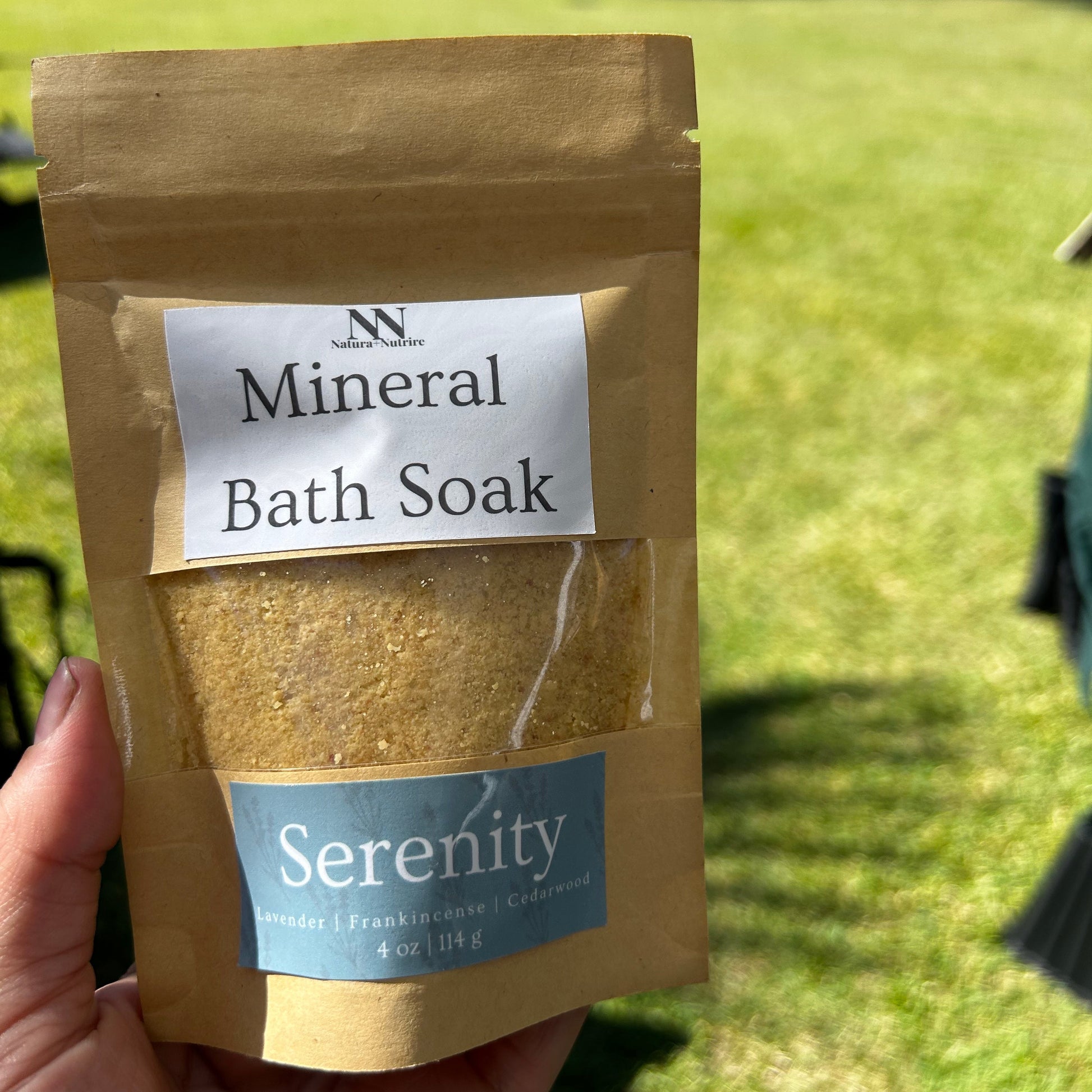 Mineral Bath Soak package labeled 'Serenity' held by a hand with a blurred green background