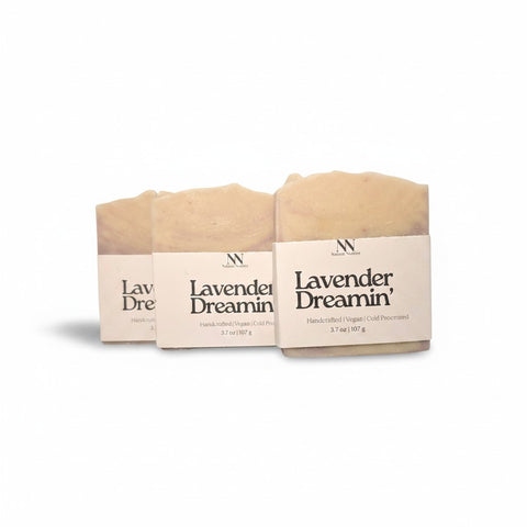 Three Lavender Dreamin' Handcrafted Soap bars wrapped in kraft paper sleeves, side by side on a white background