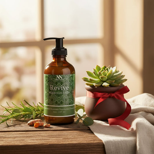Revive Magnesium Lotion pump bottle on a wooden table with a potted succulent tied with red ribbon, fresh rosemary sprigs, and turmeric root