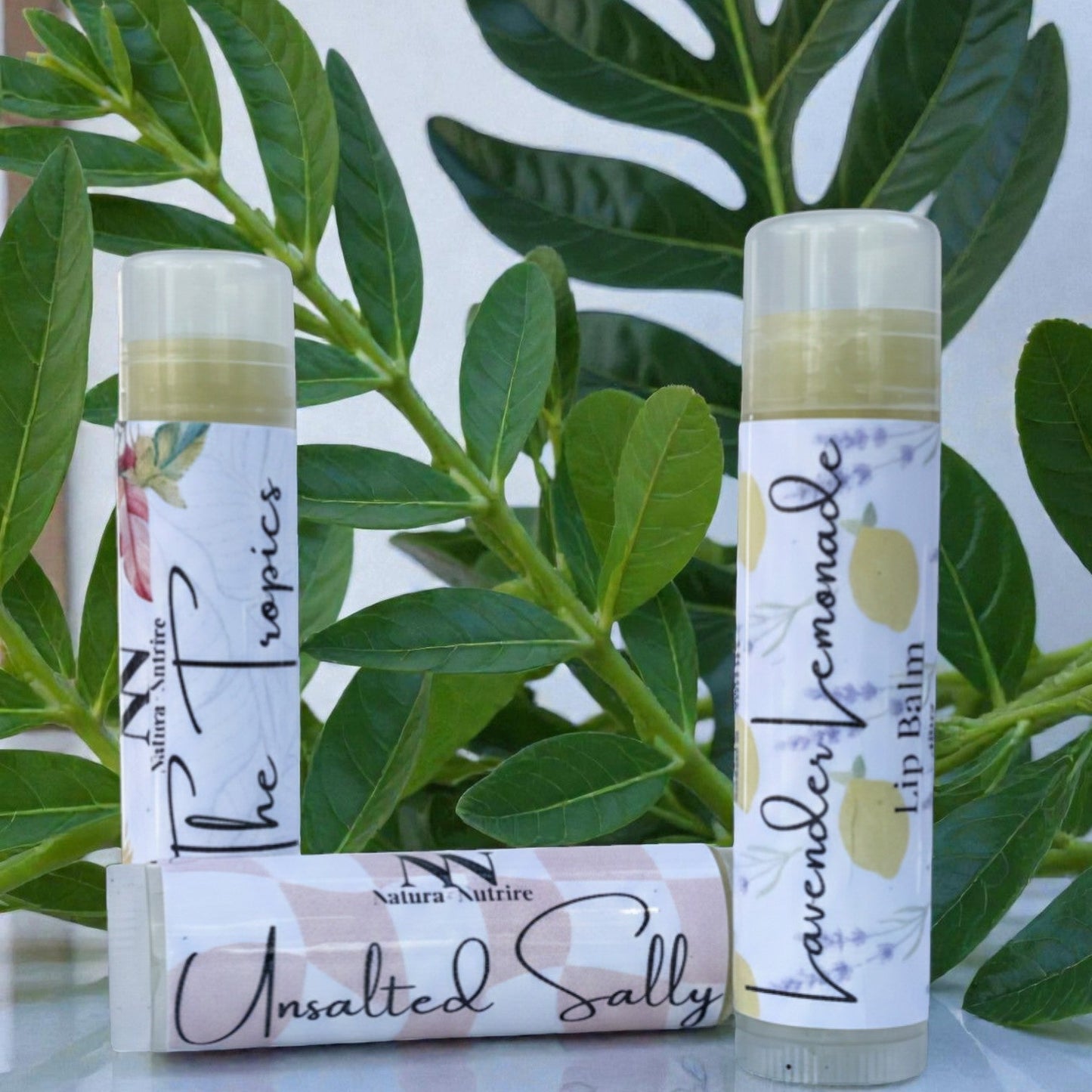 Two lip balms with labels in front of green leaves