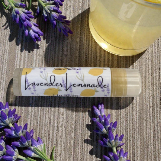 Lavender lemonade lip balm with lavender flowers and a glass of lemonade on a wooden surface