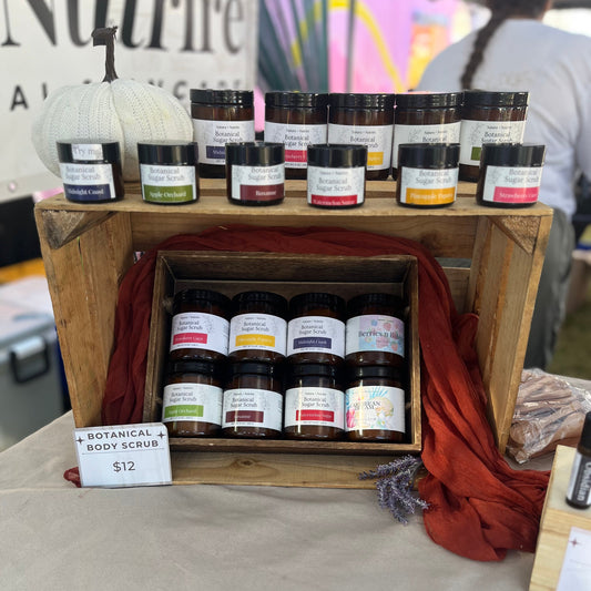 Wooden crate with various small jars labeled 'Body Scrub' on a table.