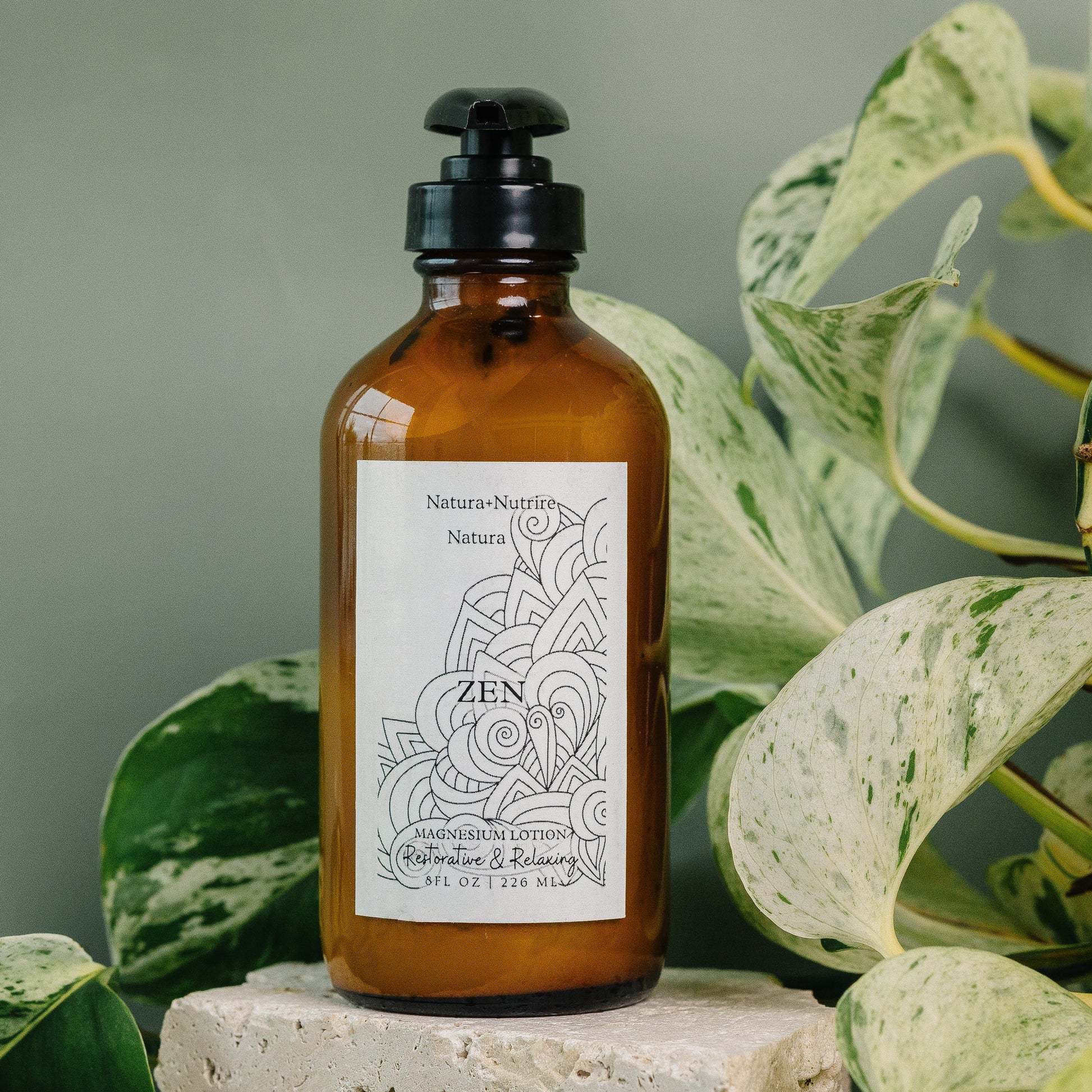 Brown bottle labeled 'Zen' with a pump on a stone surface surrounded by green leaves.